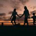 A family walks hand in hand against a vibrant sunset, evoking togetherness and peace.