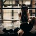 A female boxer sitting in a gym ring, resting and wiping sweat with a towel after a workout.